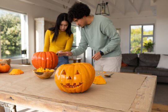African American couple carving pumpkins at home with carved jack o lantern for halloween