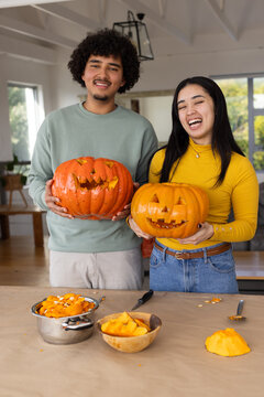 African American couple carving pumpkins and scooping seeds at kitchen table halloween