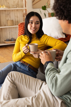 Couple sitting on light-colored couch holding ceramic mugs, woman wearing mustard top