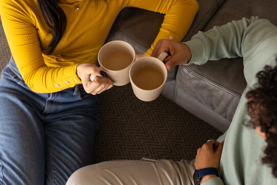 African American couple on herringbone rug by gray sofa, holding ribbed mugs, wearing pendant watch