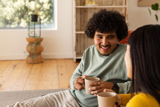 African American couple sitting on low sofa holding ribbed mugs, wearing sage-top mustard-sweater