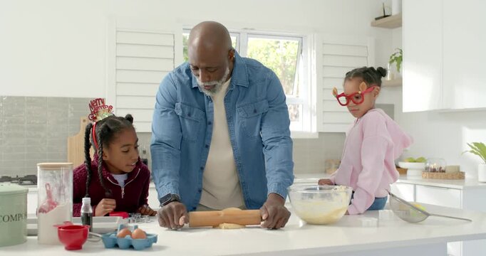 African American dad with two children rolling dough with rolling pin in kitchen for christmas