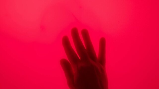 Silhouetted Hand Moving Across a Vivid Red Illuminated Background with Fingers Spread