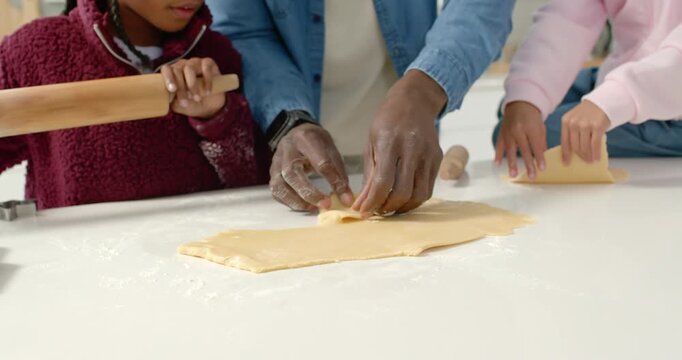 African family father guiding two children rolling dough for christmas at kitchen with wooden pin