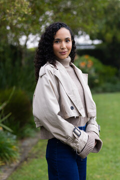 African American woman standing in garden wearing cropped trench coat and ribbed turtleneck by path