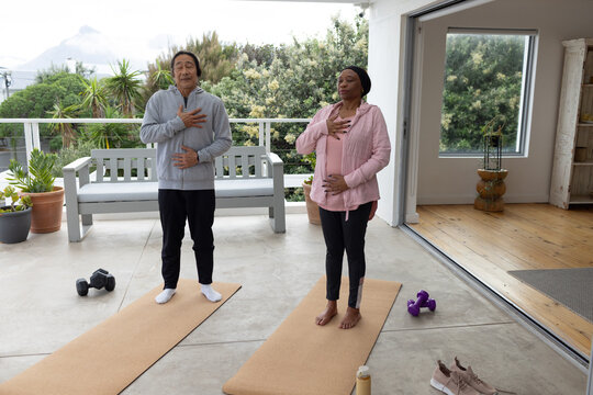 Couple Senior Asian man and woman practicing breathing on patio in activewear near dumbbells
