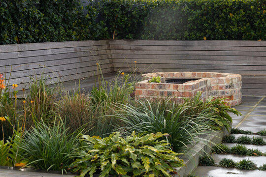 Raised planting bed is sitting in private courtyard with circular brick fire pit and timber bench