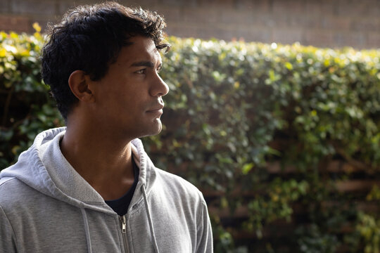 African American man standing facing right in garden wearing light grey zip-up hoodie, copy space