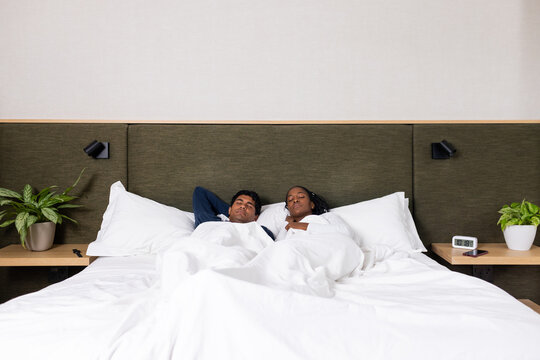 Couple lying side-by-side, resting in bedroom on king bed with duvet, bedside tables with plants