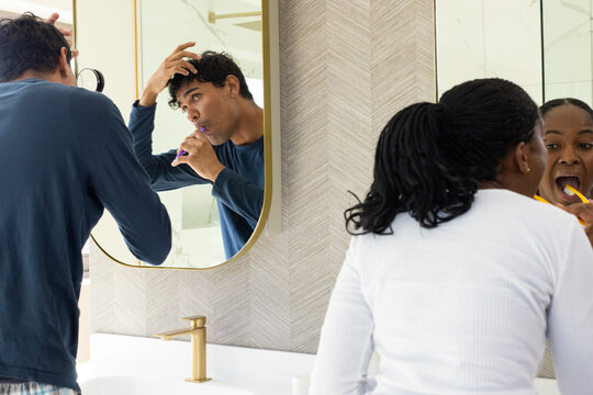 African American couple brushing teeth at bathroom vanity using purple and yellow toothbrushes