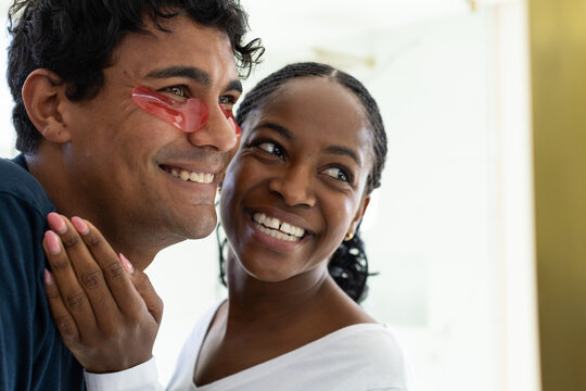 African couple smiling together at home, man wearing red hydrogel patches, woman showing pink nails