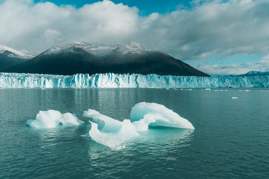 View of Perito Moreno Glacier with floating icebergs in the turquoise water, framed by snow-capped mountains under a cloudy sky in Perito Moreno, Santa Cruz Province, Argentina.