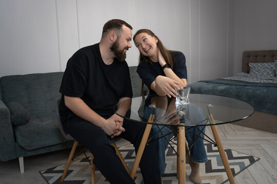 Young man and woman sitting at a glass table, engaging in a lively conversation, with the woman expressing surprise and excitement while talking with the man