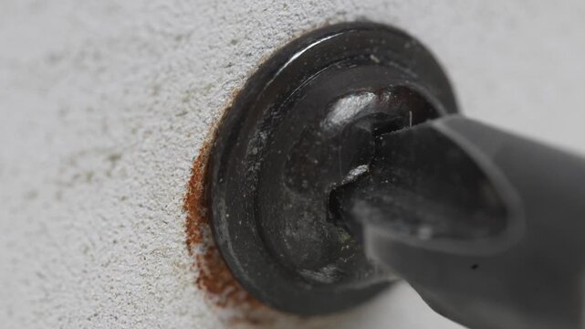 Removing the rusty black screw from the white metal using a  screwdriver.

