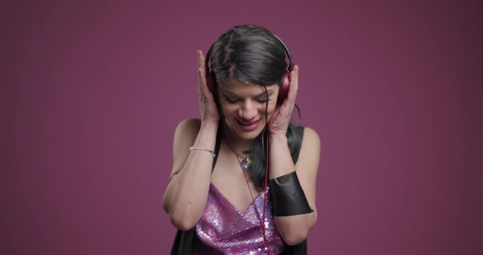Woman enjoying music with headphones, dancing in a sequin dress against a pink background