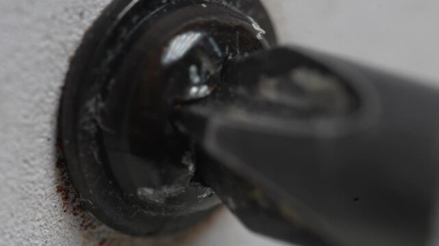 Removing the rusty black screw from the white metal using a  screwdriver.
