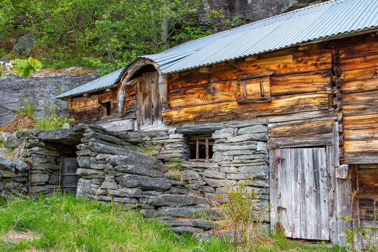 View of the historic Me-Akneset mountain farm featuring traditional wooden architecture and stone masonry walls nestled against a steep hillside in Stranda, More og Romsdal, Norway.