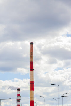 Tall striped industrial smokestack rising beneath dramatic clouds with streetlights and smaller towers visible in an urban industrial landscape