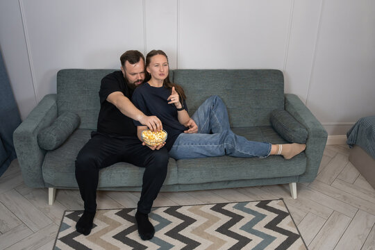 Young couple enjoying a leisure weekend evening at home, sitting on the couch and eating popcorn while watching a film together in a comfortable, relaxed setting