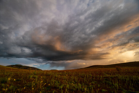 View of dramatic storm clouds over the Sacred Valley at sunset with golden light illuminating the rolling hills and grassy fields in Urubamba Province, Cusco, Peru.