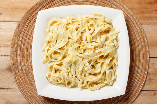 Fettuccine Alfredo with cheese sauce served on a square white plate, garnished with fresh basil, on a wooden table.