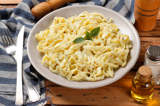 Creamy Fettuccine Alfredo served in rustic dishware, with white cheese sauce and fresh basil, on a wooden table.