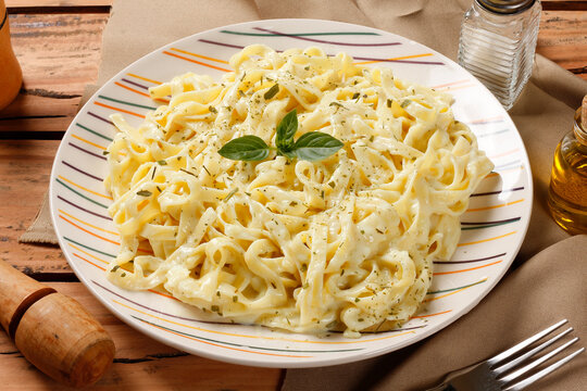 Fettuccine pasta in a creamy white cheese sauce, served on a ceramic plate with fresh basil on a natural wood surface.