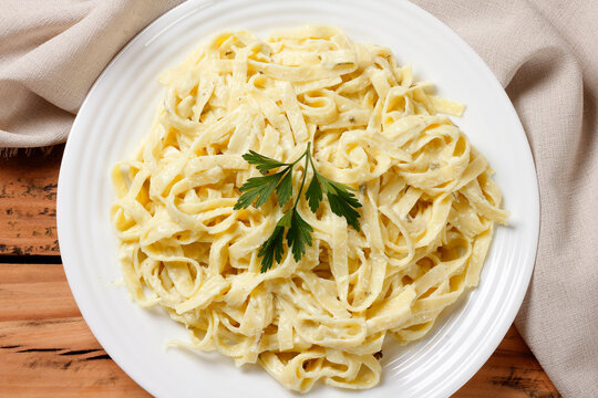 Fettuccine Alfredo served on a white plate, coated in a creamy cheese sauce, on a rustic table.