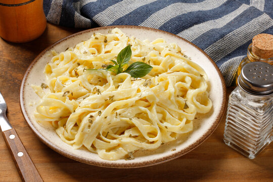 Fettuccine pasta in a white cheese sauce, served on a rustic plate with fresh basil on a wooden table.