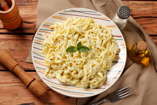 Traditional Fettuccine Alfredo with creamy white sauce on a ceramic plate, finished with green basil, on a wooden table
