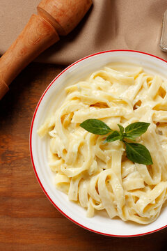 Creamy Fettuccine Alfredo with white cheese sauce served in a white bowl, finished with fresh basil, on a wooden table.