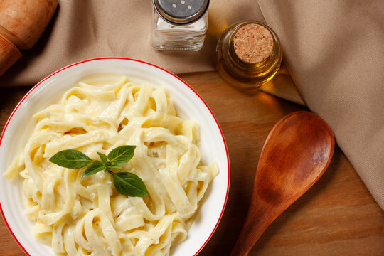 Creamy Fettuccine Alfredo with cheese sauce, served in a white bowl with fresh basil on a wooden table.