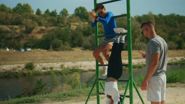 Three active men are engaged in an outdoor fitness session, with one performing a challenging inverted exercise.