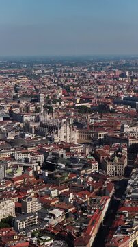 Vertical telephoto parallax view of Milan Cathedral and Piazza del Duomo in Milan, Italy, Galleria Vittorio Emanuele II dome and dense historic rooftops on a hazy sunny day