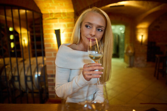 Beautiful Blonde Woman Enjoying White Wine Tasting in a Winery Cellar