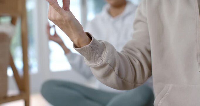 Diverse women following lead woman starting mudra, meditating on mats in hoodies at home