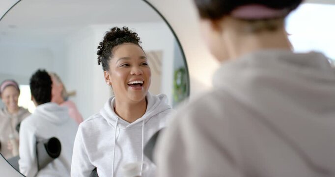 Diverse female friends coming, greeting, hugging seated woman in white hoodie by salon mirror