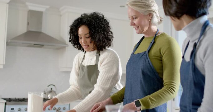 Diverse female friends following recipe left woman measuring flour into bowl at kitchen island