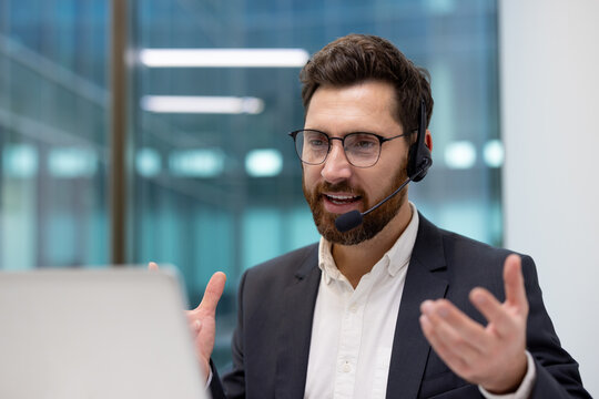 A close-up photo of a young man in a suit and headset in an office, talking on a video call and gesturing with his hands