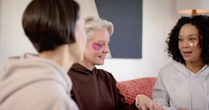 Diverse women friends on sofa, left pointing, nudging center Senior showing patches