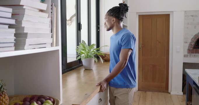 African American man leaning on kitchen counter by window, turning as cam panning, copy space