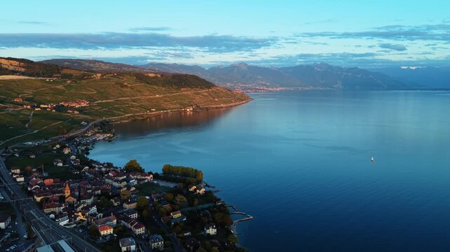 Aerial view of Cully village nestled along the terraced vineyards of Lavaux and the calm waters of Lake Geneva at sunset in Bourg-en-Lavaux, Vaud, Switzerland.