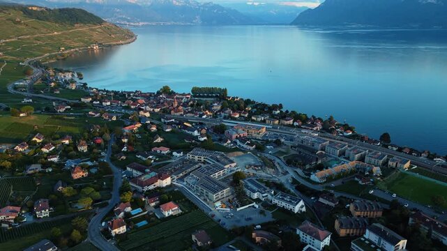 Aerial view of the town of Cully nestled along the shores of Lake Geneva with terraced vineyards and surrounding mountains in Bourg-en-Lavaux, Vaud, Switzerland.