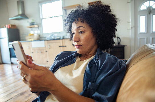 Focused woman using smartphone on couch at home