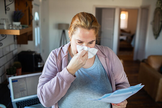 Sick woman reading bills at home with tissue