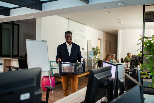 Smiling employee carrying box of belongings in office