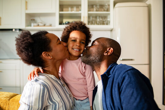 Parents kissing smiling child in home kitchen