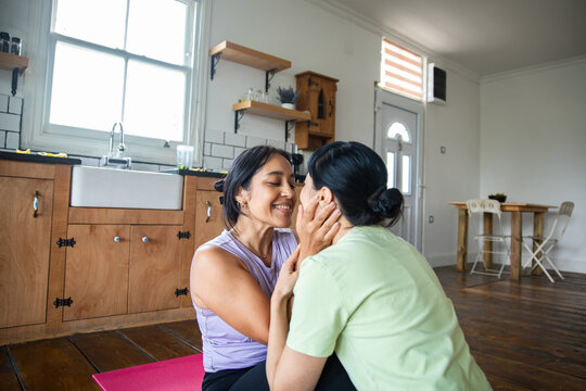 Two women cuddling on a yoga mat in a kitchen