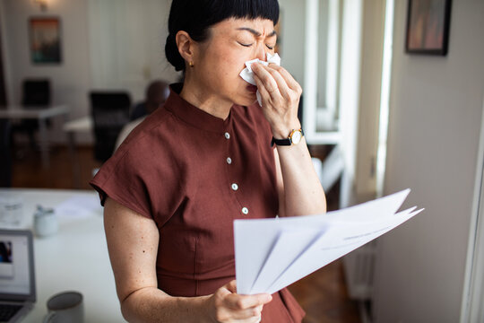 Woman blowing her nose while reading documents at work