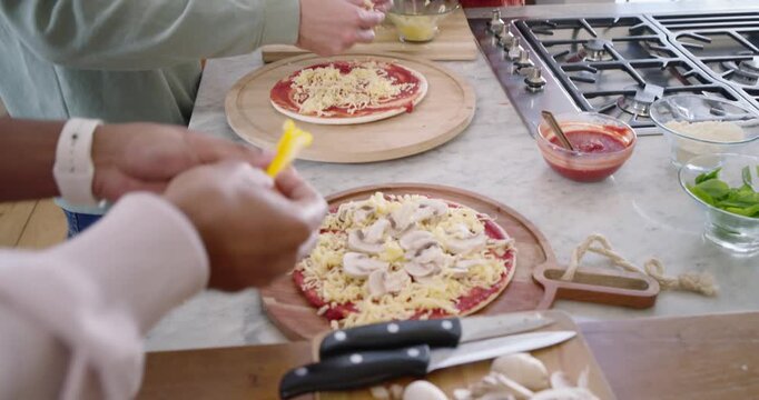 Diverse friends deciding dinner, assembling pizzas at kitchen counter using pizza peels for dinner